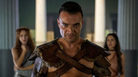 Ashur stands between two women, who are in the background