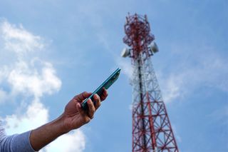 A person using a phone with a 5G mast in the background 