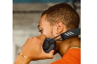 In this image a pair of the best headphones for cycling, the Adidas RTP-01 headphones, are about to be put on by a man with short hair in an orange t-shirt and is side on, he is holding the left side headphone in his hand