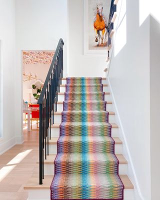 A right, rainbow-colored runner climbs the staircase surrounded by white walls