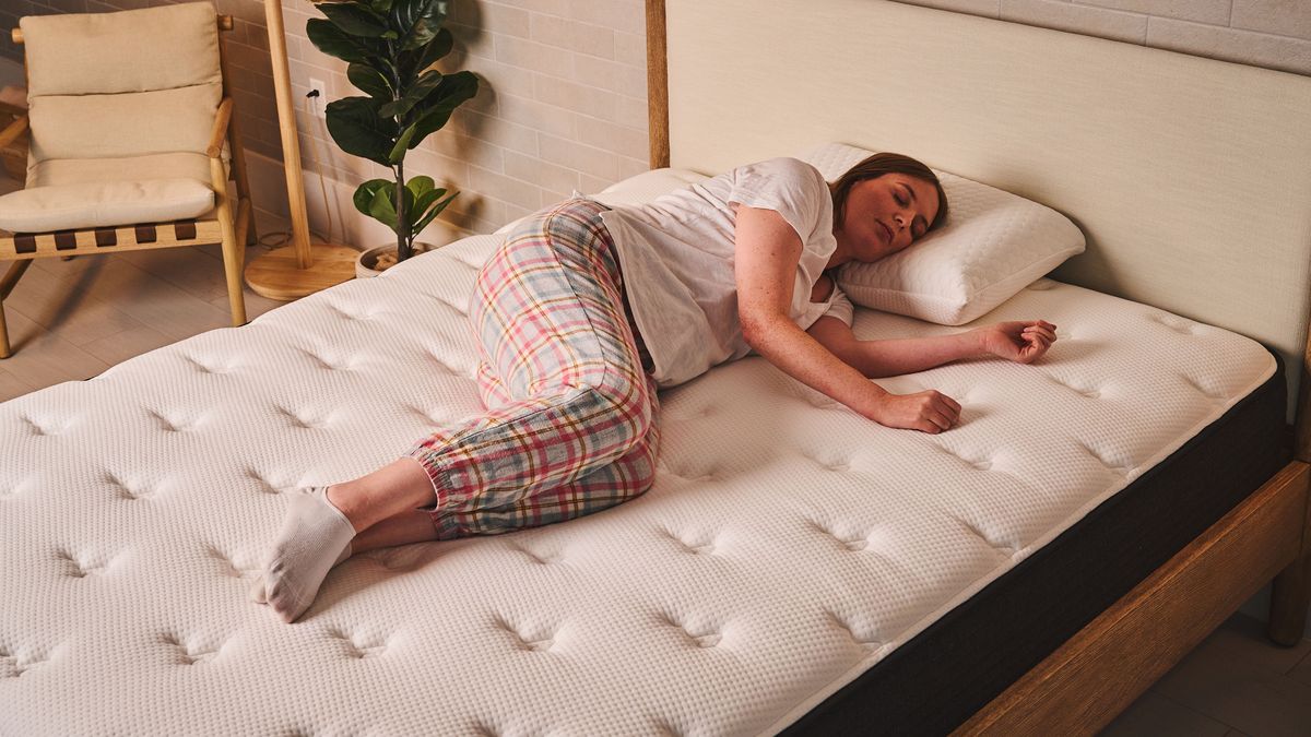 A woman lies in a side sleeping position on a Plank Firm mattress in a bedroom