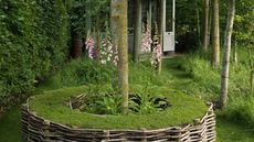 garden with round turf seat and green trees and flowers