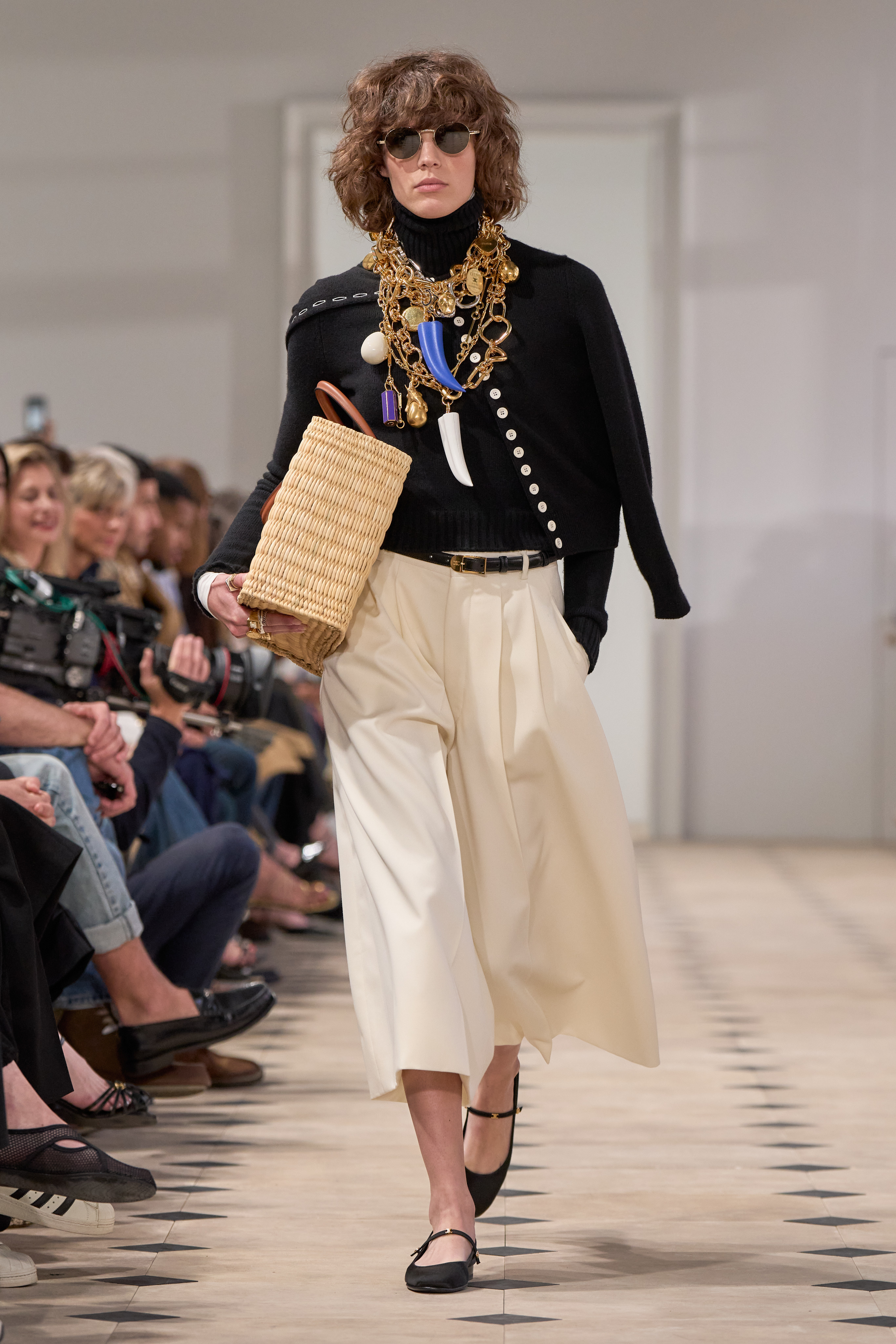 a Celine model walks down the runway wearing capris and a cardigan sweater with stacked necklaces