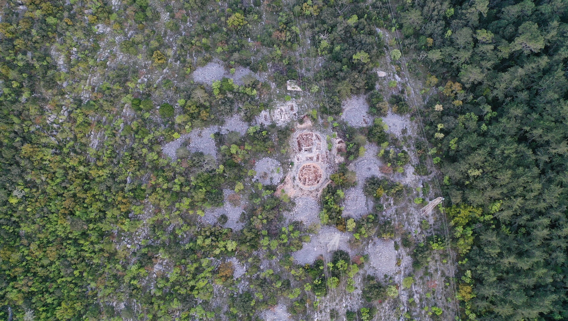 Aerial view of a mound necropolis in Croatia. We see a lot of trees and some bare stone patches.