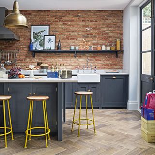Kitchen with dark grey cabinetry, parquet wooden flooring, bar stools and exposed brick wall