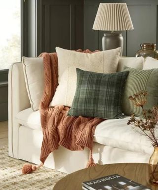 A white couch with an assortment of pillows and blankets in fall colors