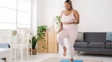 A woman exercises on a mat in a living room. She is lifting one leg off the ground. 