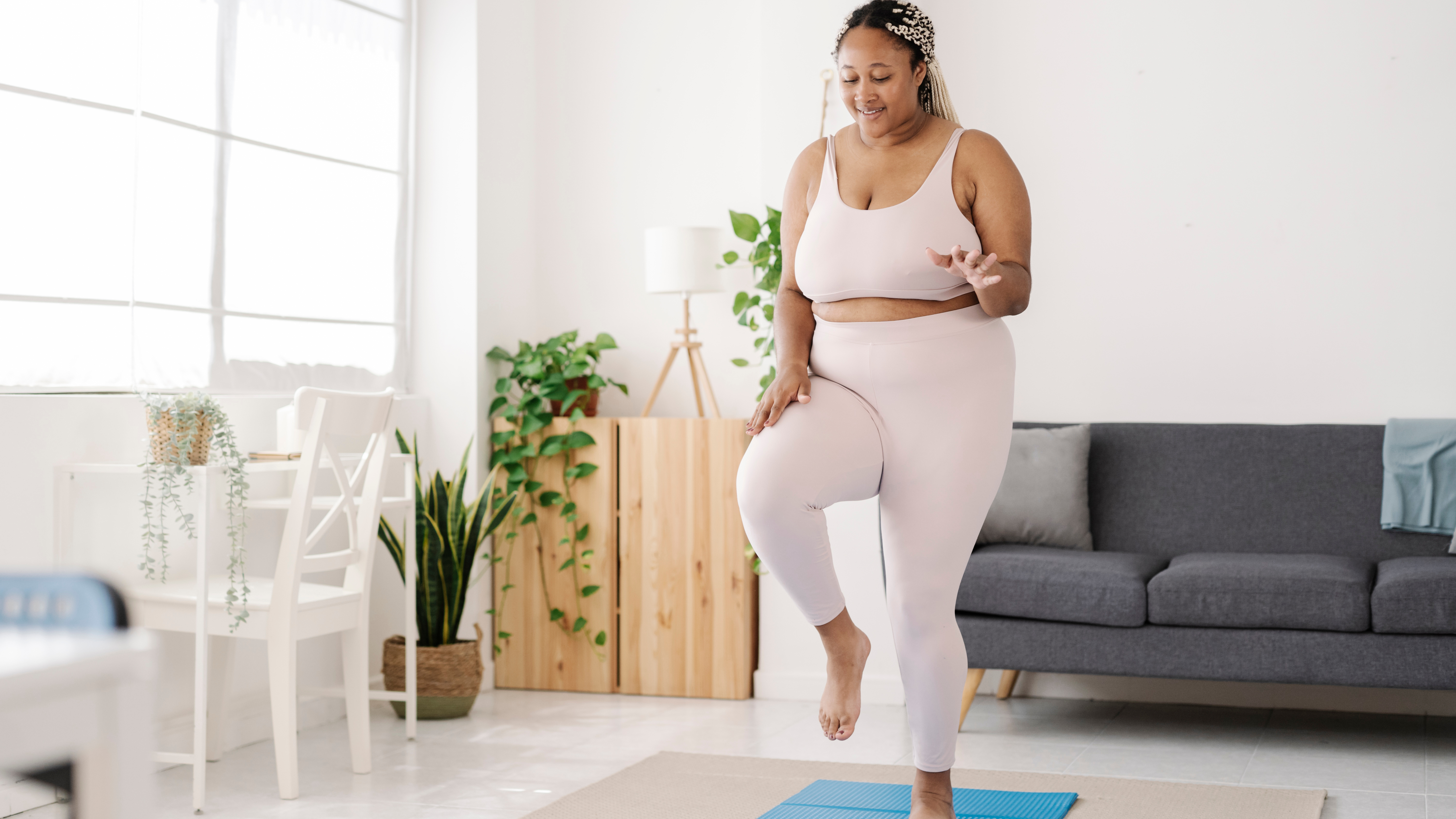 A woman exercises on a mat in a living room. She is lifting one leg off the ground. 