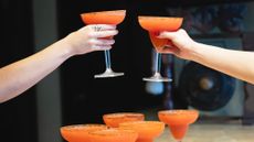 The arms of two friends engaged in a cheerful toast, each holding a glass of strawberry daiquiri.