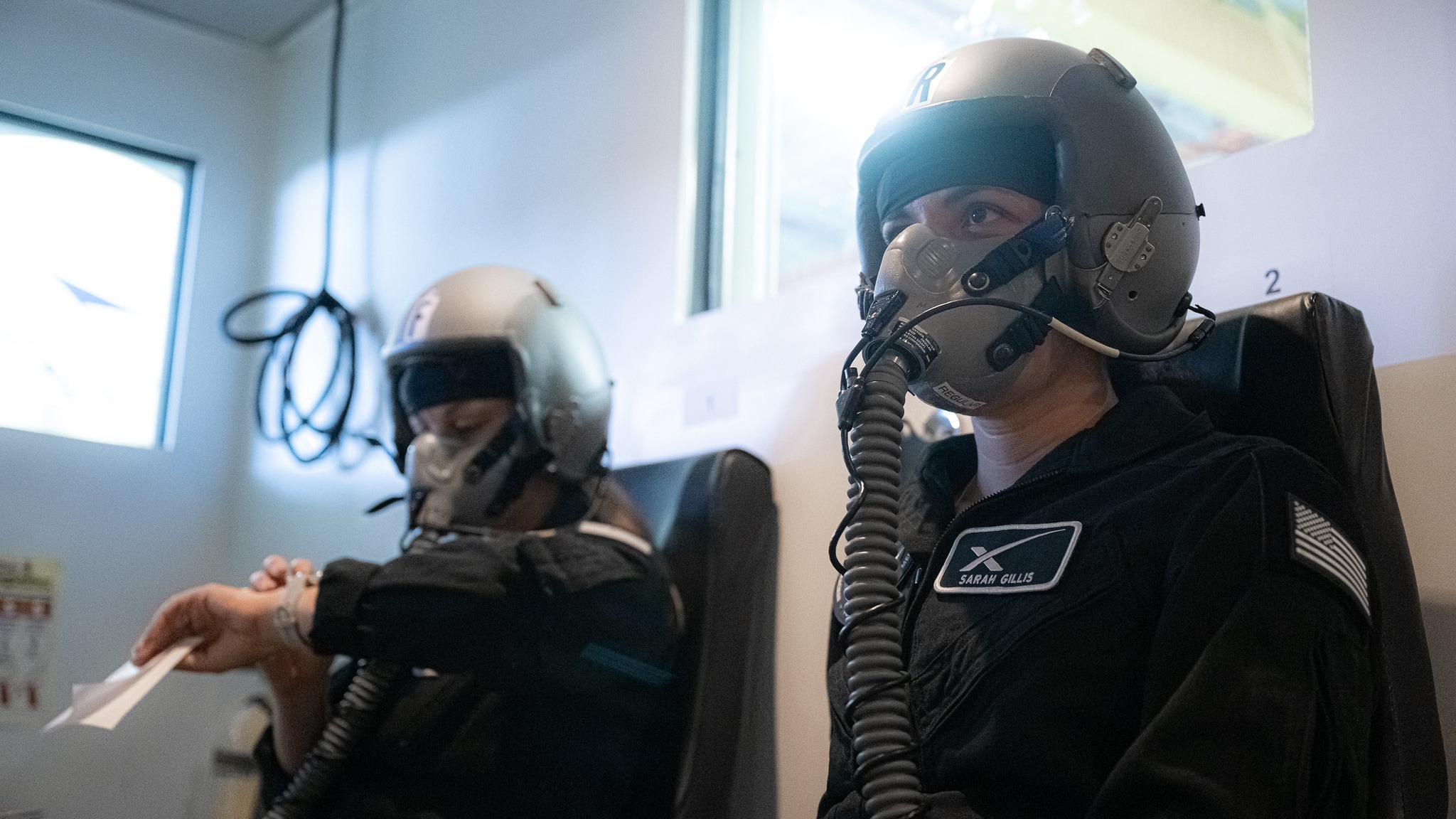 two people in black outfits and helmets doing flight training in a room