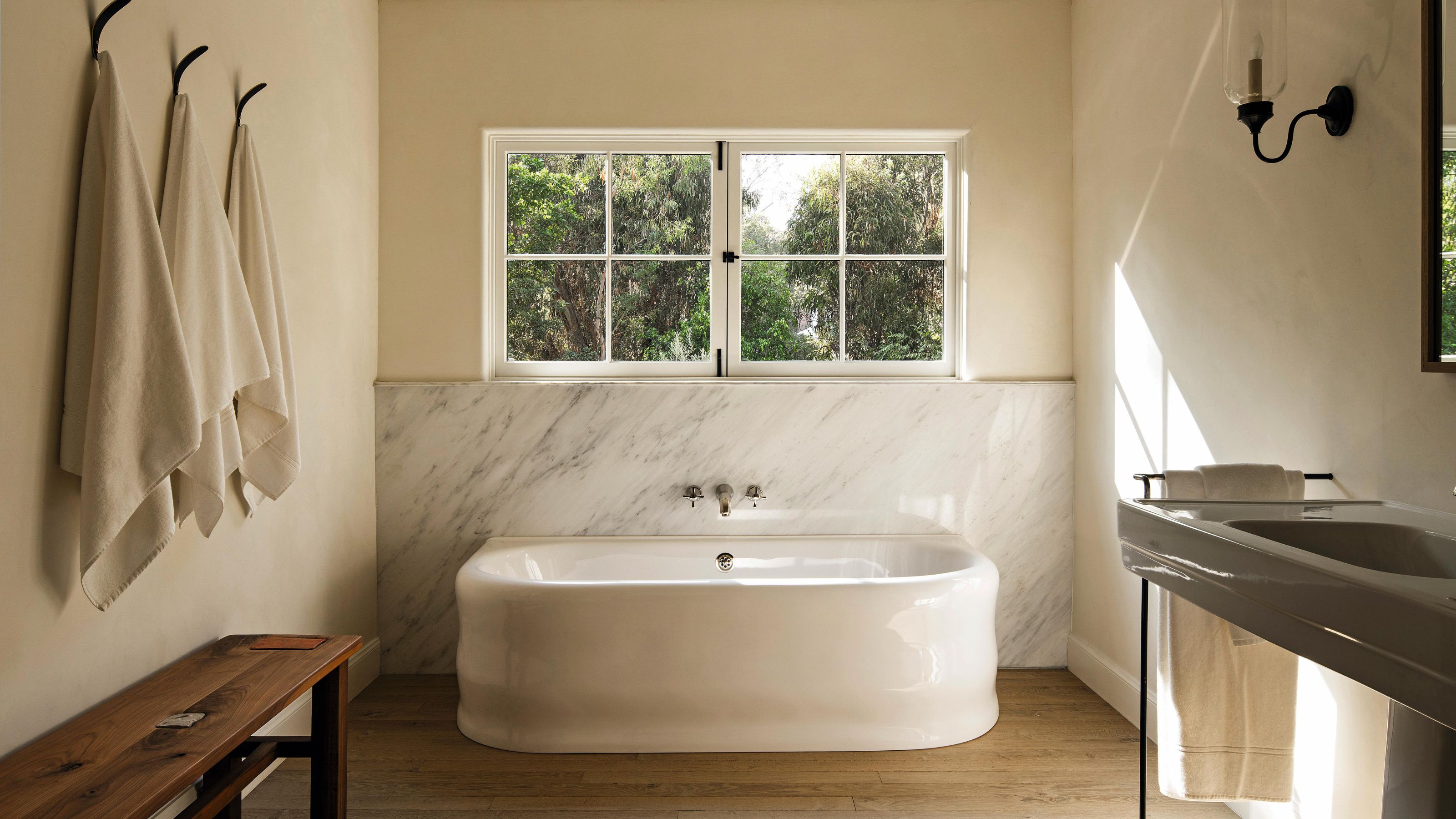 a soft neutral bathroom with a curved freestanding, mrable backsplash and simple styling