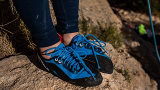 A pair of feet wearing blue and black Unparallel Up Lace climbing shoes.
