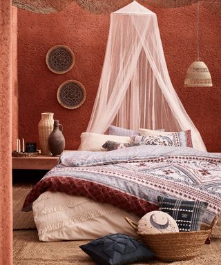 terracotta plastered walls with bed dressed in rich coloured fabrics and white canopy above bed