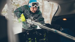 Young man packing his skis in the trunk of the car