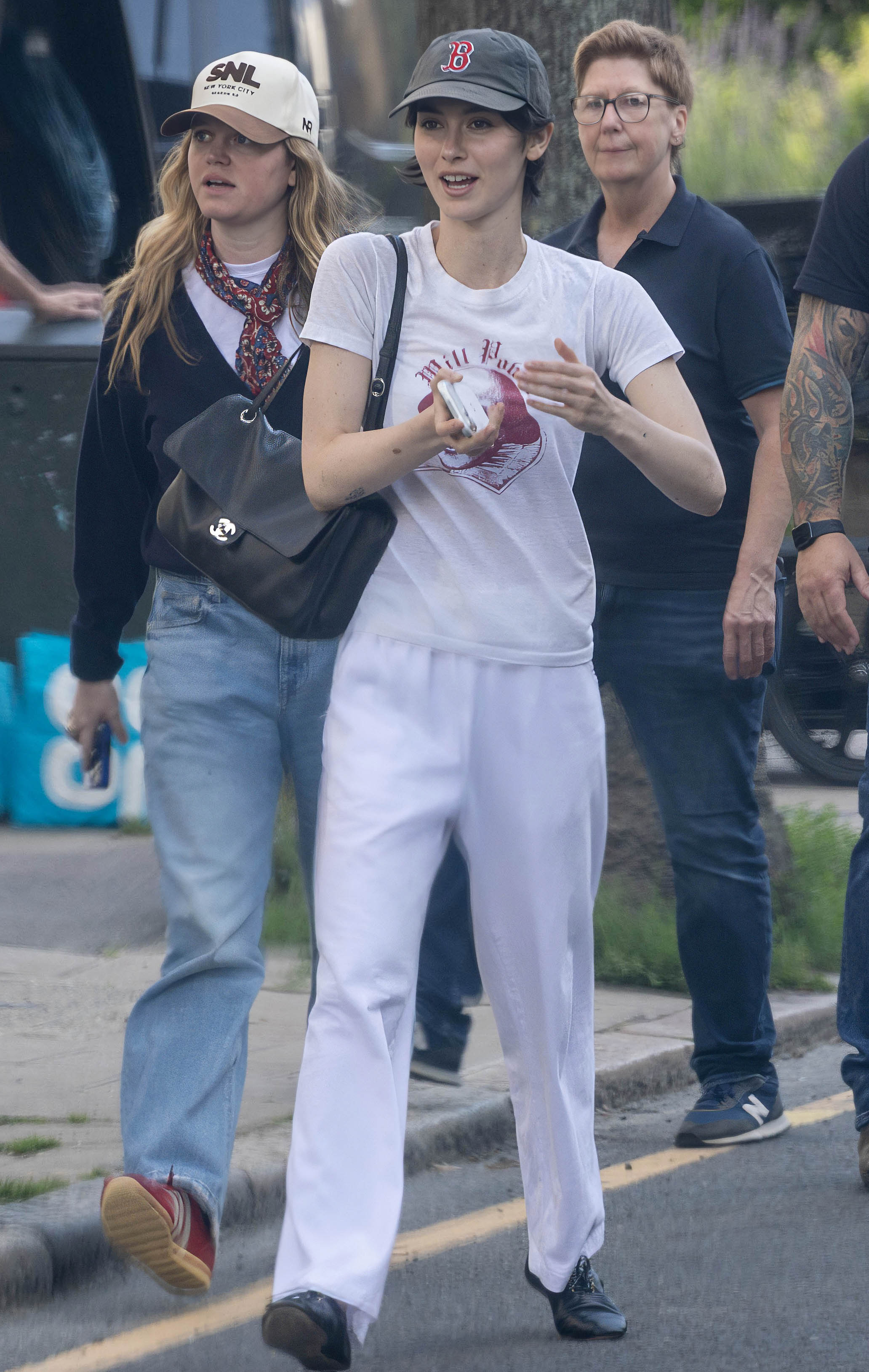 Gracie Abrams wears a baseball cap, a graphic tee, a Chanel bag, white pants, and black jazz shoes.