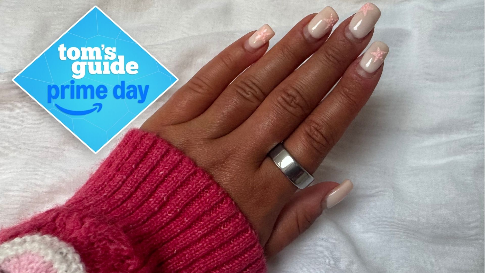 A woman&#039;s hand with pink nails and a pink sleeve wearing silver Oura Ring 4 on index finger with Tom&#039;s Guide Prime Day logo 