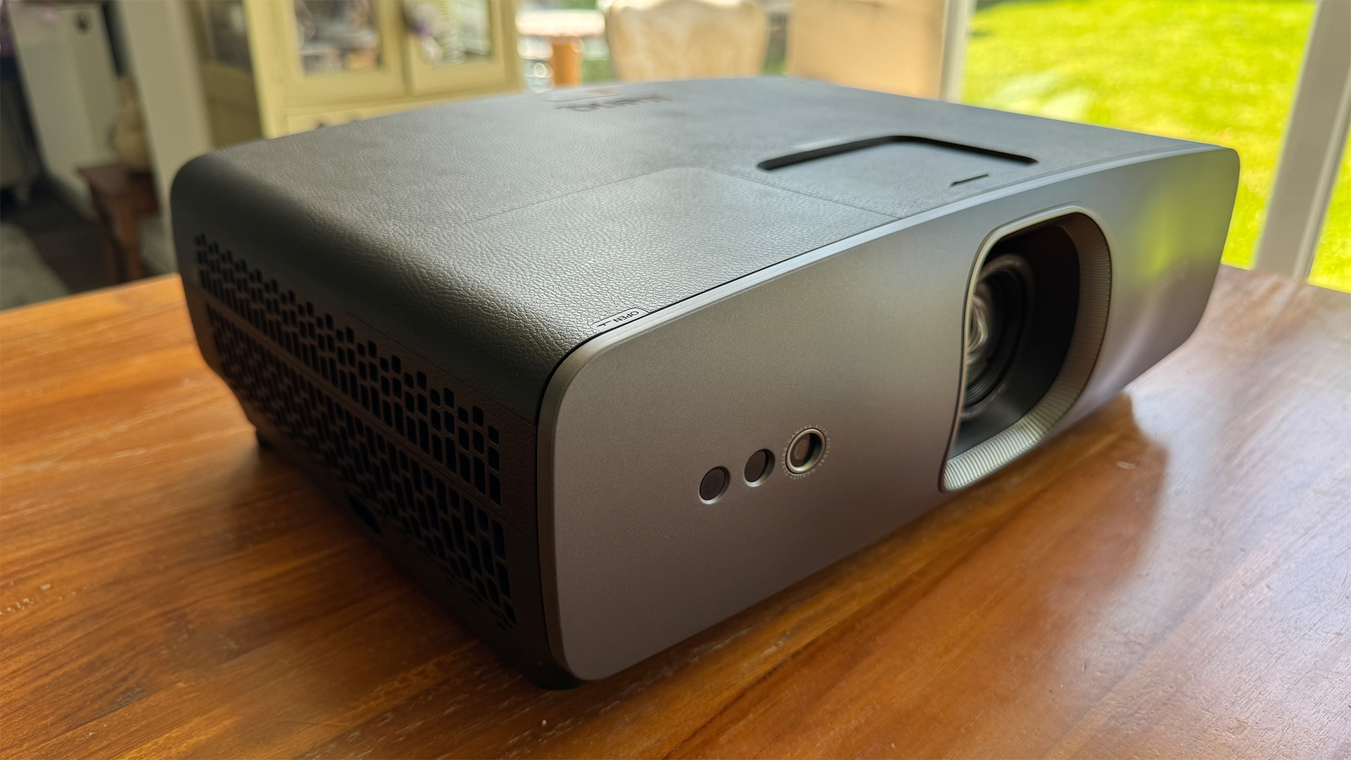 The BenQ W2720i projector, pictured on a wooden table in a living room