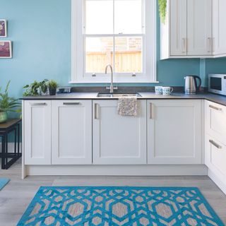 White kitchen with painted blue walls and matching blue rug.
