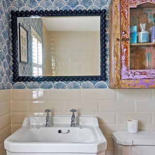 white sink underneath blue and white tiles with mirror and storage cabinet