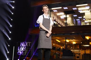 Contestant Toby in white top and grey apron in front of the kitchen in Next Level Chef.