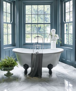 Blue bathroom decor with pastel blue window panes in bathroom with white freestanding bath and bust figurine