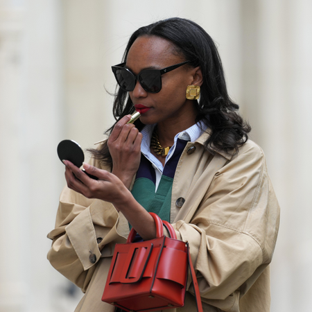 silk press Emilie Joseph wears sunglasses, golden earrings and necklace, a green and blue striped polo shirt, a white shirt, a beige oversized trench coat, a red leather bag, during a street style fashion photo session, on April 21, 2024 in Paris, France. 