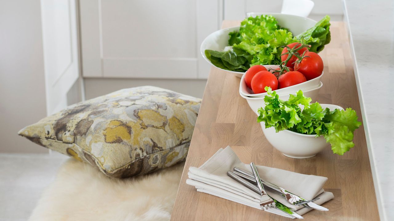 Lettuce leaves and tomatoes in white bowls on wooden table next to napkins and cutlery