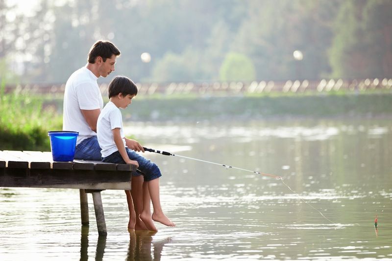 A dad and his son sit on the end of a pier, fishing