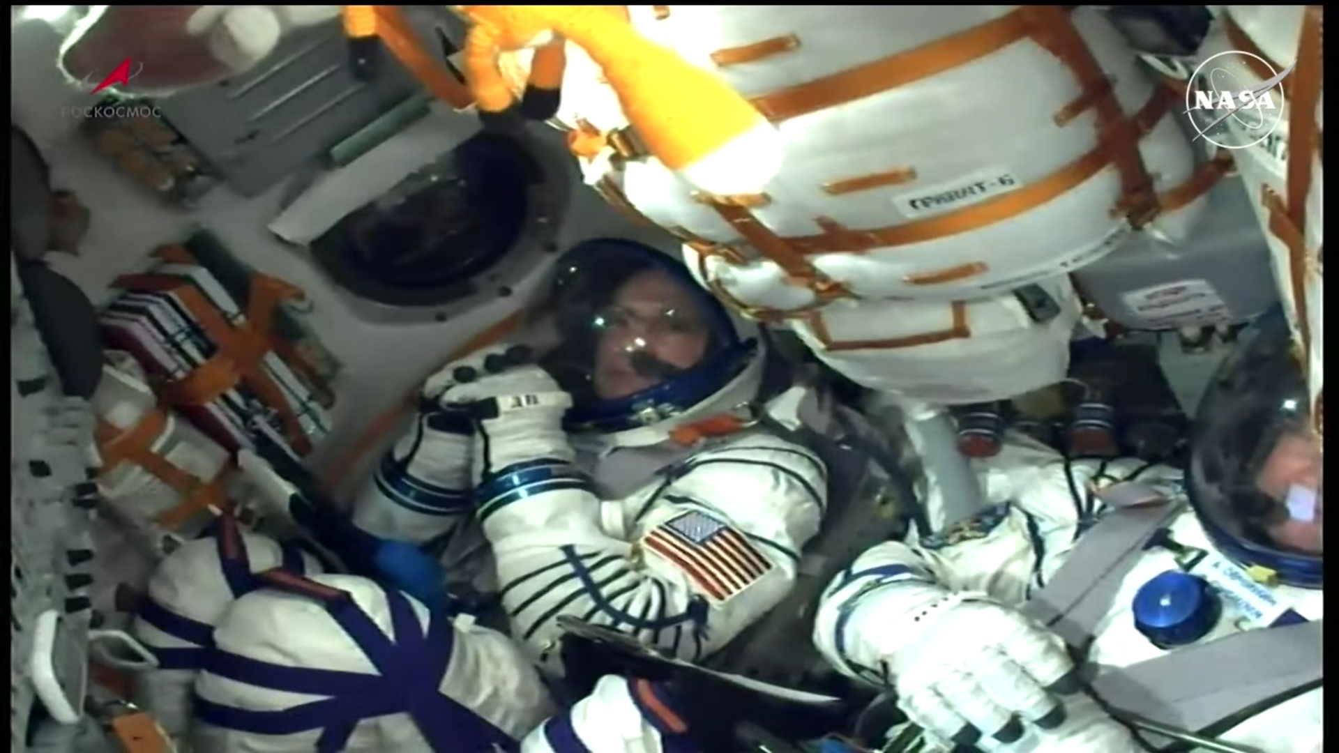 Astronauts in white spacesuits stand in a white airlock