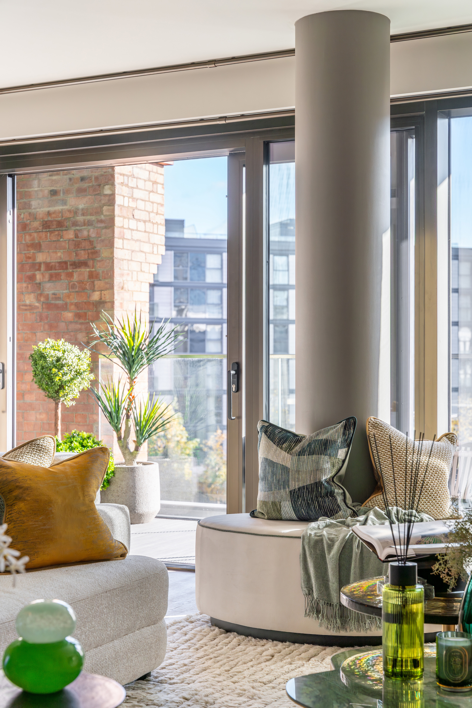 modern living room with balcony, structural column with bench seat around it, gray sofa with yellow cushion, white rug, coffee table with room diffuser, and cushions and throw on the benchseat