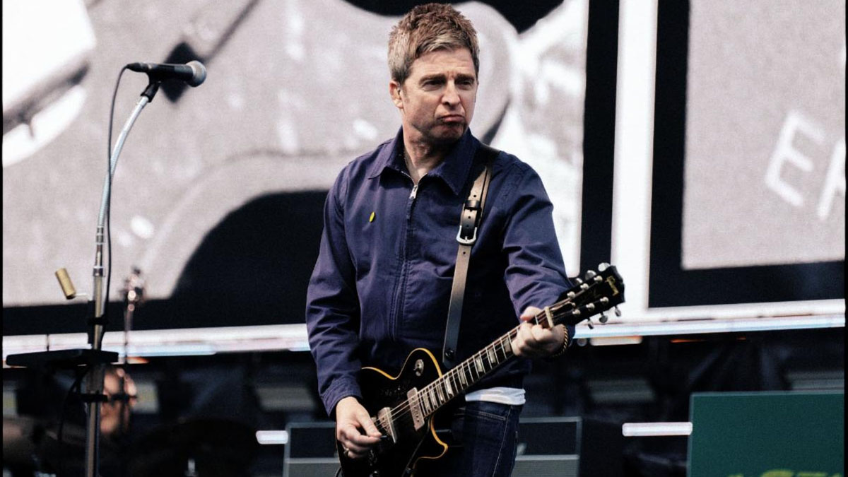 Noel Gallagher wears a navy jacket and plays his custom Gibson Les Paul Standard live onstage with Oasis in 2025.