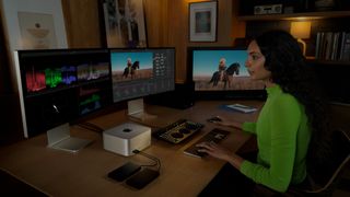 A woman sitting at a desk and editing on three screens using a Mac Studio