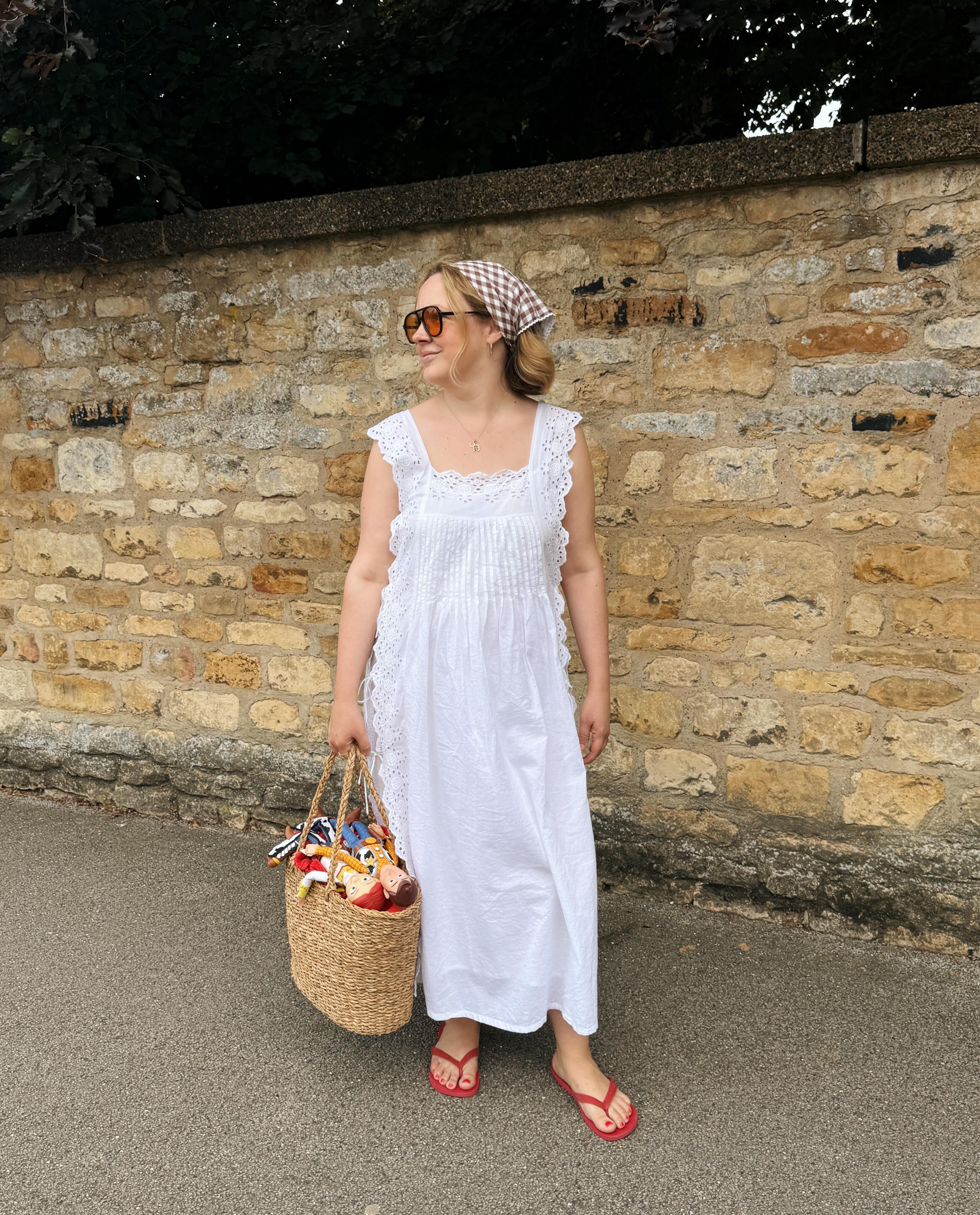 Influencer Charlotte Jackline wearing a white broderie anglaise dress, red flip flops, straw basket bag and gingham head scarf.