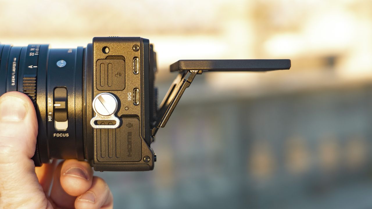 Side view of the Sigma FP2 mirrorless camera in user's hand, at golden hour outdoors, the screen is tilted up