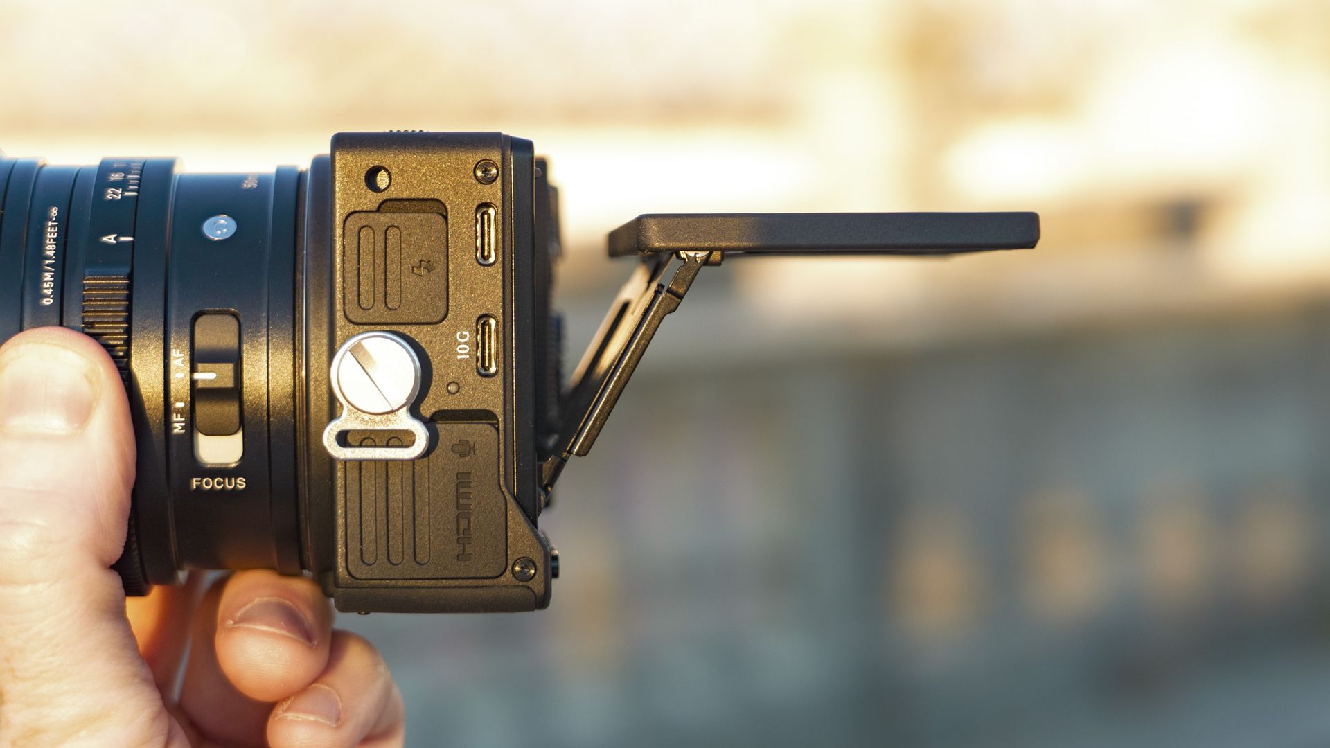 Side view of the Sigma FP2 mirrorless camera in user's hand, at golden hour outdoors, the screen is tilted up