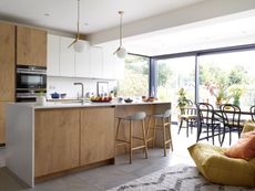 open-plan kitchen-diner and living area with handless wooden cabinets, grey bar stools and glazing