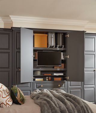 TV in built in shelving unit in bedroom, doors to hide, grey cabinetry