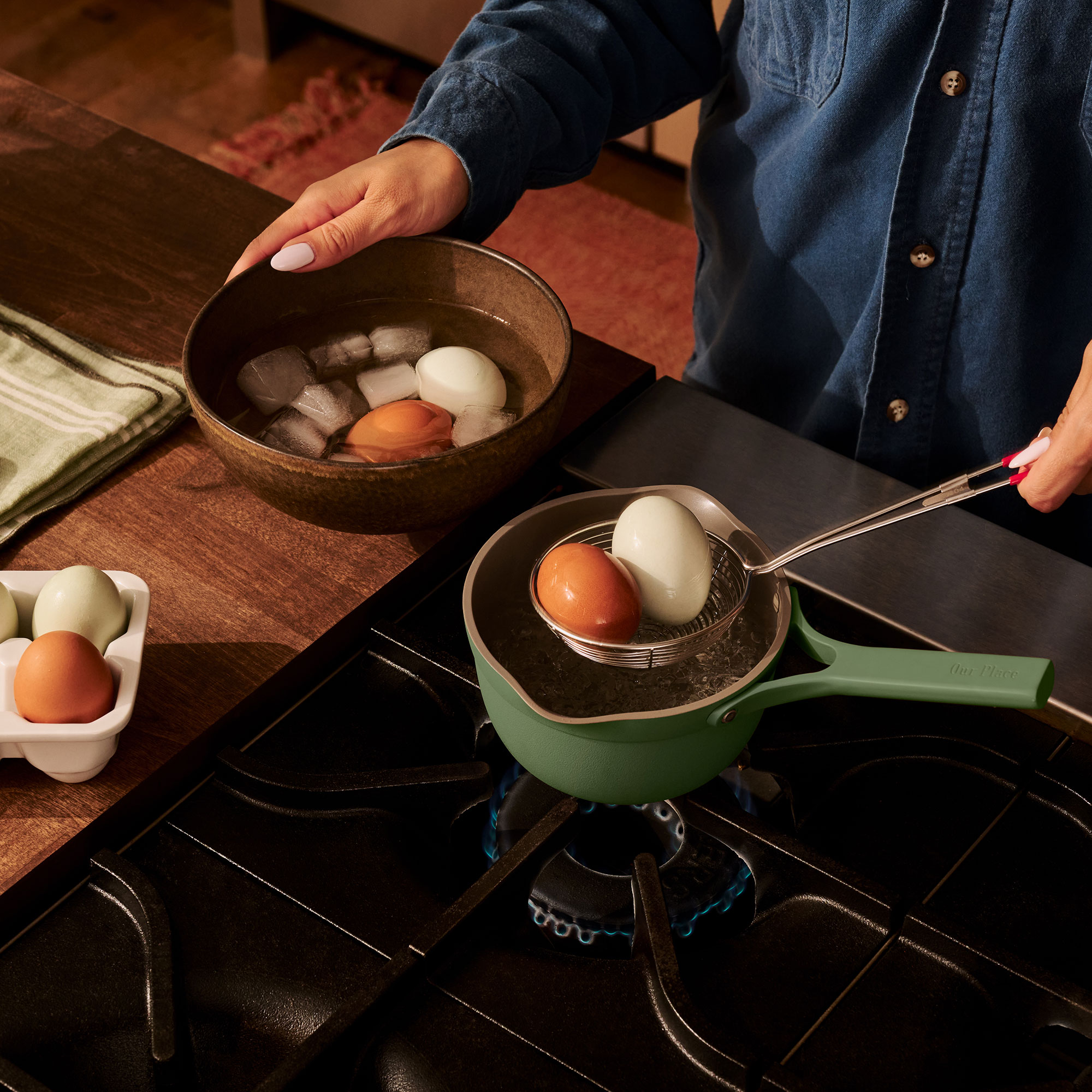 Person taking two eggs out of small green pan sitting on hob burner