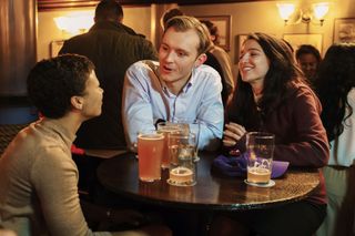 Harper (Myha'la), Robert (Harry Lawtey) and Yasmin (Marisa Abela) sit around a table in a pub, with pint glasses of varying fill levels in front of them, all looking happy