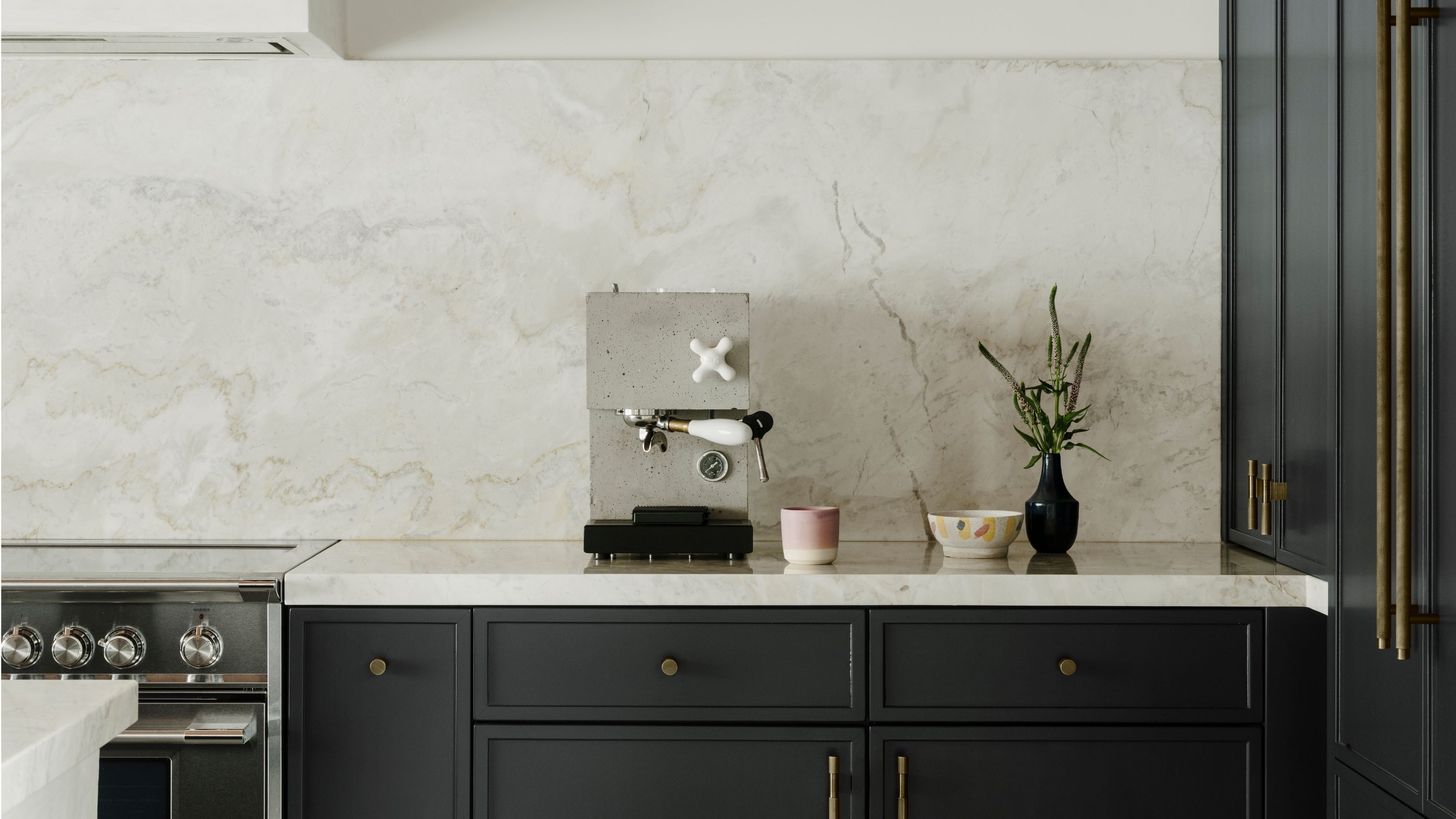Image of a concrete coffee machine on a white marble countertop that matches the backsplash and black cabinetry underneath.