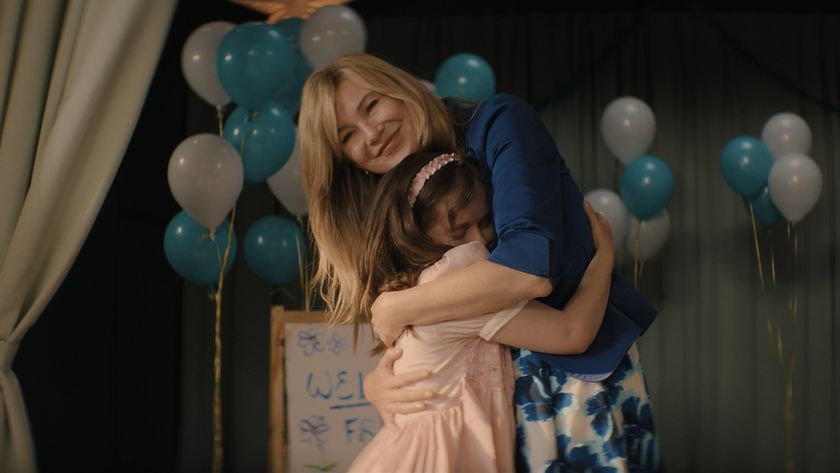 A beaming Kristine Barnett (Ellen Pompeo) embraces her newly adopted daughter Natalia (Imogen Faith Reid) on a stage filled with pastel pink and blue balloons in Good American Family.