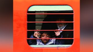 Child making hand gestures behind red bars of a train window