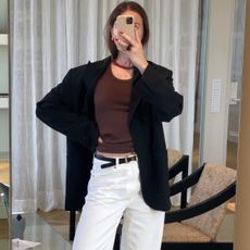 Swedish fashion pr and influencer Johanna Lager poses for a mirror selfie wearing a red beaded necklace, brown basic top, oversize black blazer, thin black belt, and white jeans