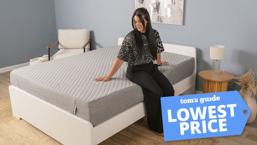 A woman sits on the edge of the Siena Memory Foam Mattress in a bedroom, testing the edge support of this cheap gel memory foam mattress. A Tom's Guide lowest price deals graphic in the right corner