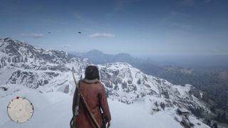 Red Dead Online - A player stands on top of a snowy mountain looking at a valley down below.