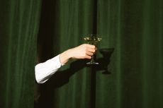 A man's arm protrudes from behind a curtain holding a martini