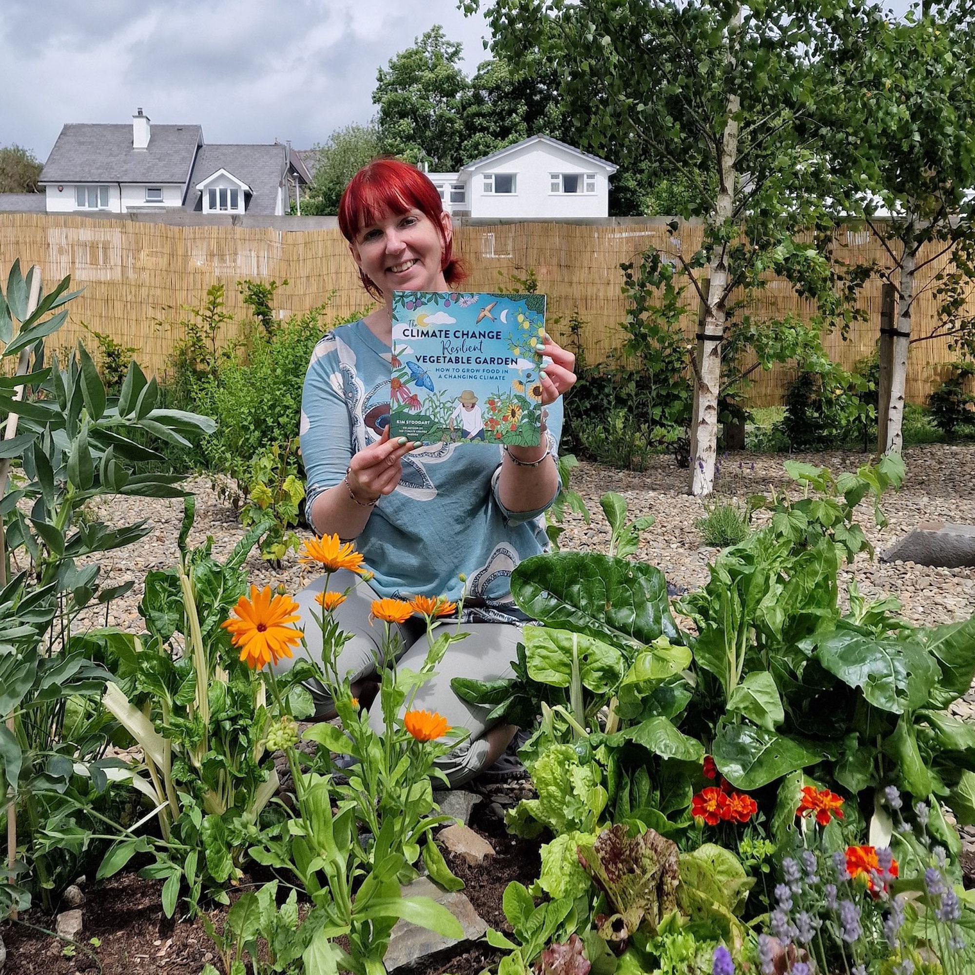 Kim Stoddart, environmental journalist holding a book on front of plants at Creuddyn community garden