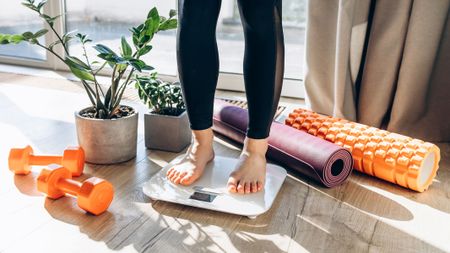 Image shows a woman standing on a smart scale with exercise equipment in the background