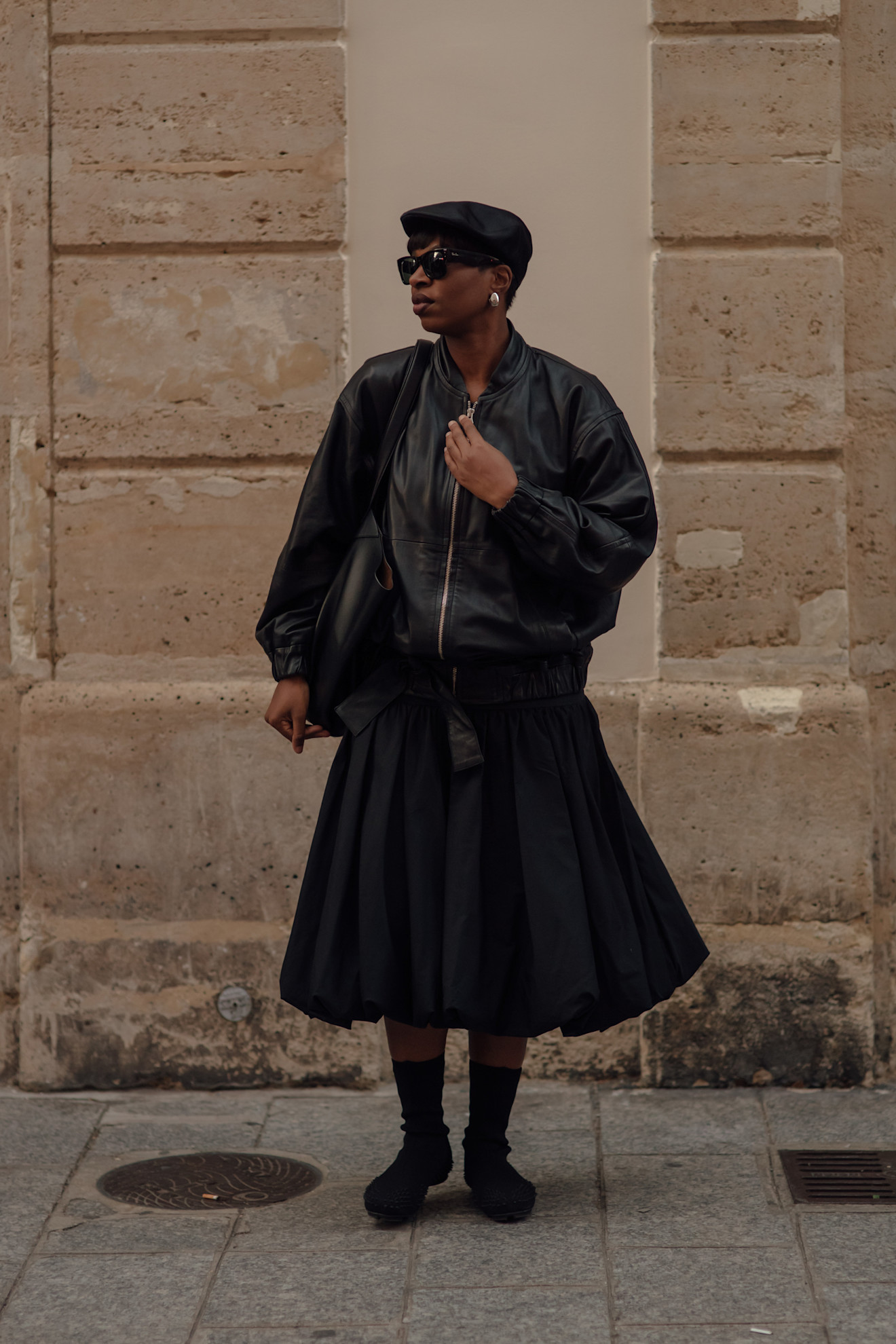 Woman in a midi skirt, a black leather jacket, a hat, and flats