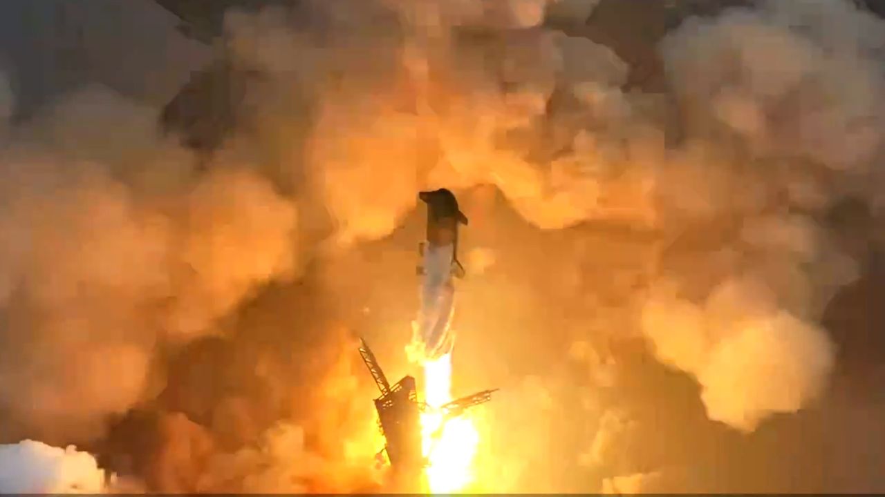 a large silver-and-black rocket launches above a plume of fire